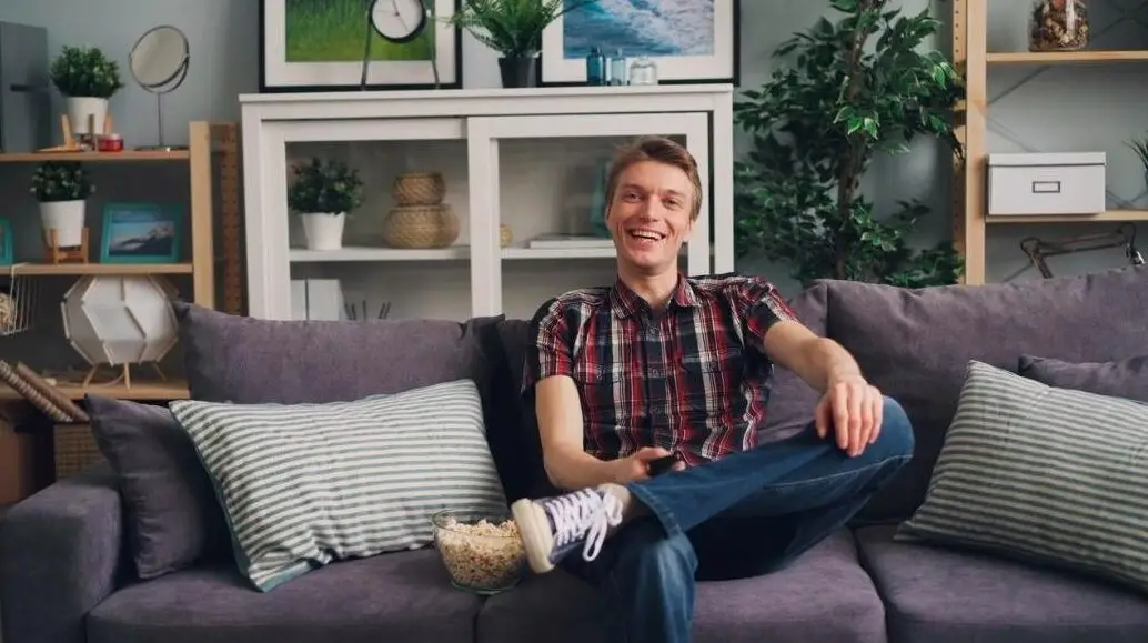 A cheerful man sits on a sofa with popcorn, enjoying his leisure time in a stylish living room.