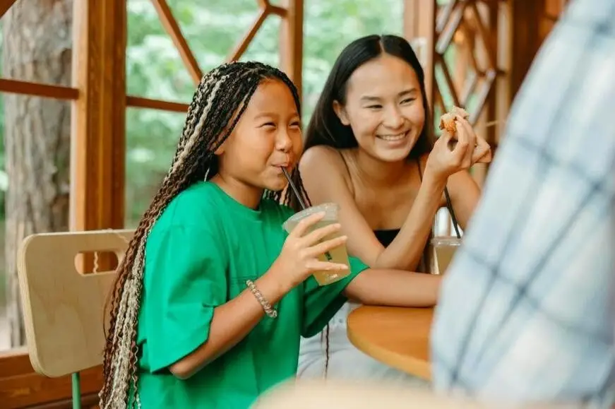 A mother and daughter enjoying a fun meal together in a bright café with wooden interior.